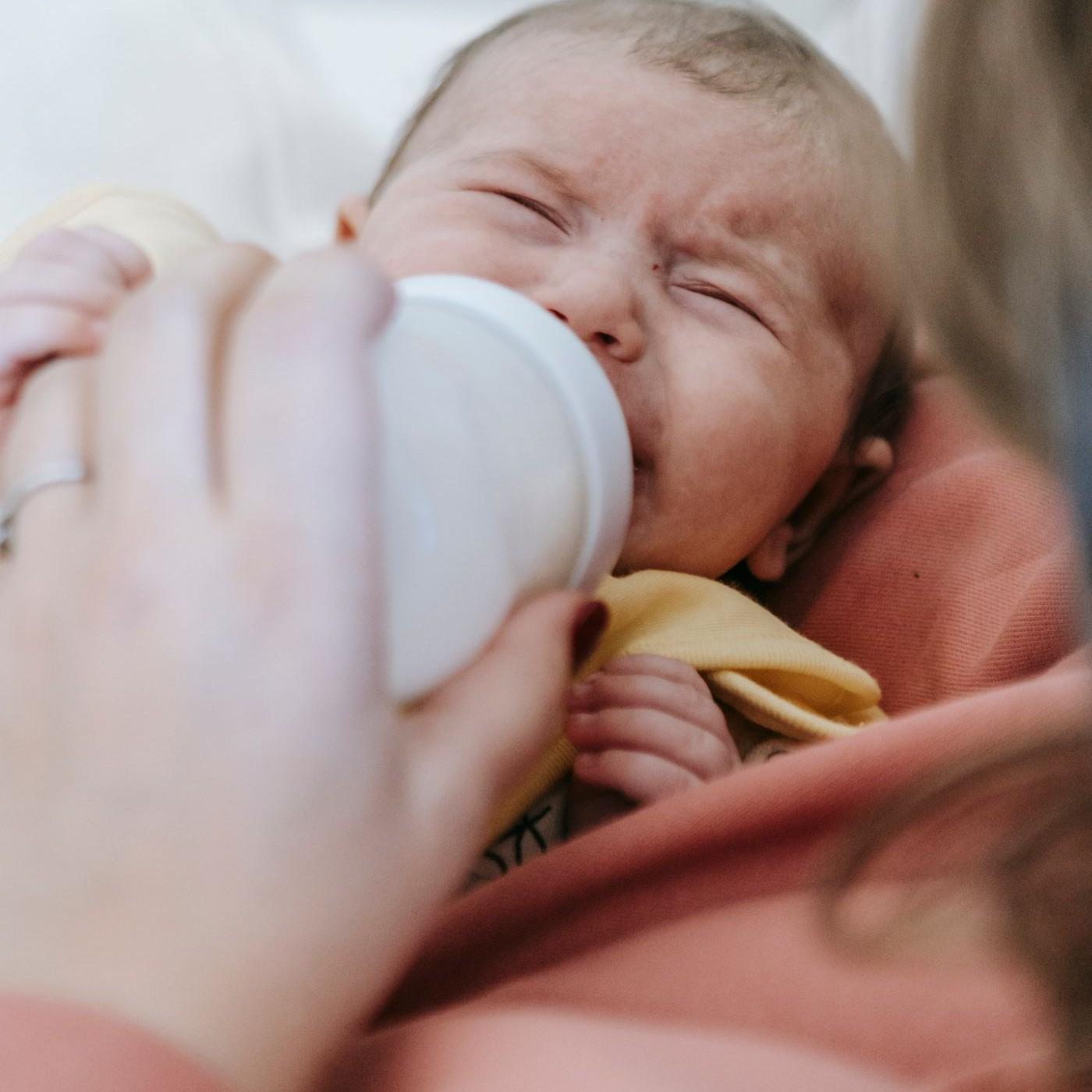 A parent holding a crying baby while offering a bottle.